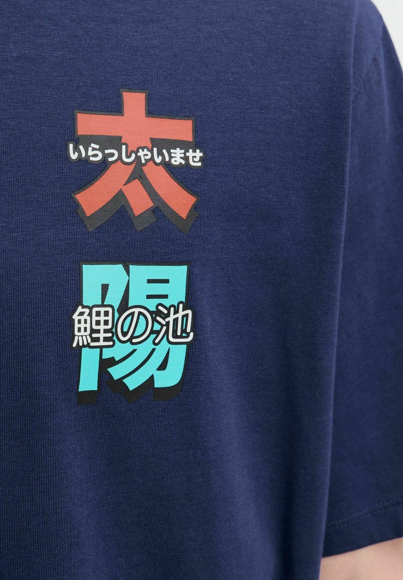 Camiseta de algodón azul marino con texto japonés impreso en colores rojo y aqua. Textura suave, mangas cortas y diseño de cuello redondo.