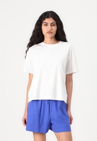 Hvit bomulls t-skjorte med korte ermer og avslappet passform, sammen med blå shorts med snøring. Enkelt design og glatt tekstur.
