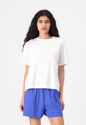 Witte katoenen T-shirt met korte mouwen en een relaxte pasvorm, gecombineerd met blauwe shorts met trekkoord. Eenvoudig ontwerp en een soepele textuur.