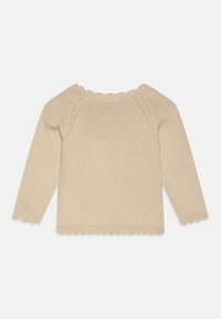 Bežani pleteni pulover s dugim rukavima, valovitim izrezom i rubom. Ima glatku teksturu, uski oblik i rebraste manšete.