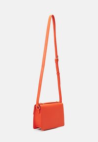 Oranžová kožená křížová taška s obdélníkovým tvarem, nastavitelné ramenní popruhy a zlatými kovovými akcenty. Hladká textura a minimalistický design.