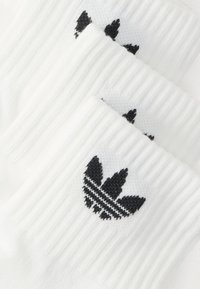 Meias brancas de algodão com o logótipo Adidas trefoil bordado a preto. Textura canelada com acabamento suave, empilhadas em três camadas.