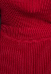 Gros plan sur un tissu en tricot côtelé rouge avec des motifs de couture horizontaux et verticaux et un détail de couture plié.