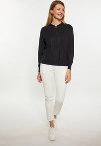 Černá mikina na zip s kapucí, s šňůrkou, žebrovanými manžetami a lehkým materiálem, spárovaná s bílými slim-fit kalhotami a bílými teniskami.