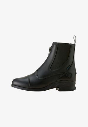 Bottine en cuir noir avec fermeture éclair latérale, panneau élastique, petit talon et détails de marque sur le côté extérieur.