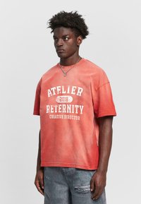 T-shirt en coton à gradient rouge avec des manches courtes, comportant un texte imprimé blanc : "ATELIER RETERNITY 2018 DIRECTEUR CRÉATIF." Coupe décontractée.