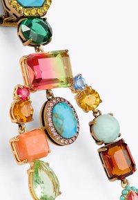 Gioielli in tonalità oro che presentano varie gemme colorate, tra cui smeraldo, turchese e rosa, con montature intricate e forme diverse.