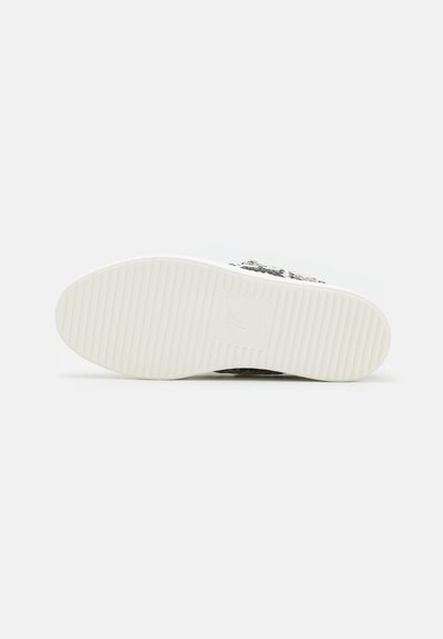 Semelle de sneaker en caoutchouc blanc avec des rainures texturées et un branding subtil. La tige présente un design à motifs en noir et gris.