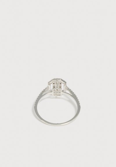 Bague en argent avec un sertissage à plusieurs griffes tenant une grosse pierre précieuse centrale, photographiée sur fond blanc uni.