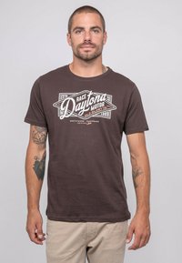 T-shirt en coton marron foncé avec un graphique vintage en blanc représentant Daytona Motor sur le devant. Manches courtes et col rond.