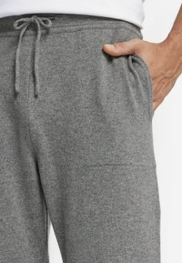 Grå fleecebyxor med elastisk midja, dragsko och sidofickor. Tyget ser mjukt och texturerat ut, lämpligt för avslappnad användning.