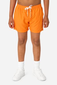 Feloranje zwembroek met een elastische tailleband en witte trekkoord. Glad textuur, opgerolde zomen en zijzakken. Draagt wit sneakers en sokken.