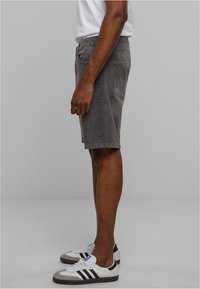 Pantalones cortos de mezclilla gris con corte recto, que cuentan con cinco bolsillos y detalles de costura lateral, llevados con zapatillas blancas y grises.