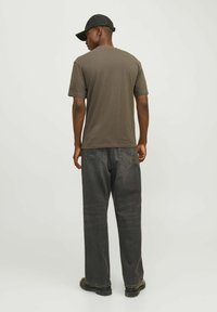 Brun t-shirt med korte ærmer, parret med mørkegrå lige ben jeans. Personen bærer en sort caps og står mod en lys baggrund.