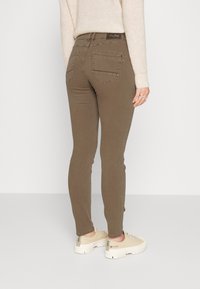 Jeans skinny marrones con cintura alta, bolsillos traseros y un acabado texturizado sutil, combinados con zapatillas beige claro.