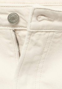 Jeans din denim alb cu un buton argintiu și fermoar pe față. Țesătură texturată distinctă cu cusături tonale și un bucle pentru curea.