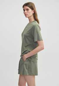 Top de manga corta color verde oliva con cuello redondo, textura suave y corte relajado, combinado con pantalones cortos a juego que cuentan con bolsillos laterales.
