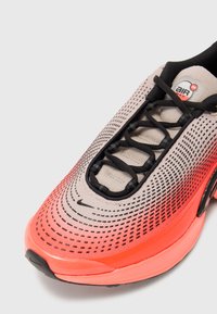 Nike Air Max sportiniai bateliai pasižymi gradientiniu dizainu, pereinančiu nuo kreminės iki ryškiai oranžinės spalvos, tekstūruotu tinkliniu viršumi, juodu raiščių sistemu ir paminkštintu apykakle.