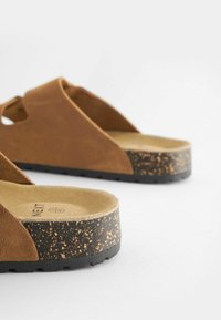 Smeđe suede klizne sandale s čepovim uloškom i teksturiranom crnom gumom; s otvorenim dizajnom i naglascima od prirodnih materijala.