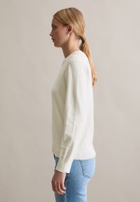 Crèmekleurige trui met ronde hals en lange mouwen, met geribbelde manchetten en zoom, gecombineerd met lichtblauwe spijkerbroek. Soepele textuur en casual pasvorm.