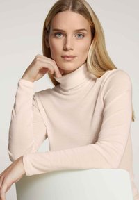 Light pink turtleneck top with a soft, ribbed texture and fitted sleeves. The fabric appears lightweight and smooth, with a high neck design.