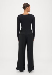 Melnas garām piedurknēm bodijs ar apaļu kakla izgriezumu, kas pārī ar platajām melnajām biksēm, kurām ir aizmugurējās kabatas un aproce.