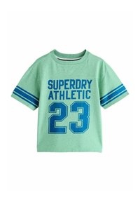 Zaļš kokvilnas T-krekls ar īsām piedurknēm, ar uzrakstiem "SUPERDRY ATHLETIC" un "23" biezā zilā tipogrāfijā. Piedurkņu maliņas ar svītrām zila krāsā.