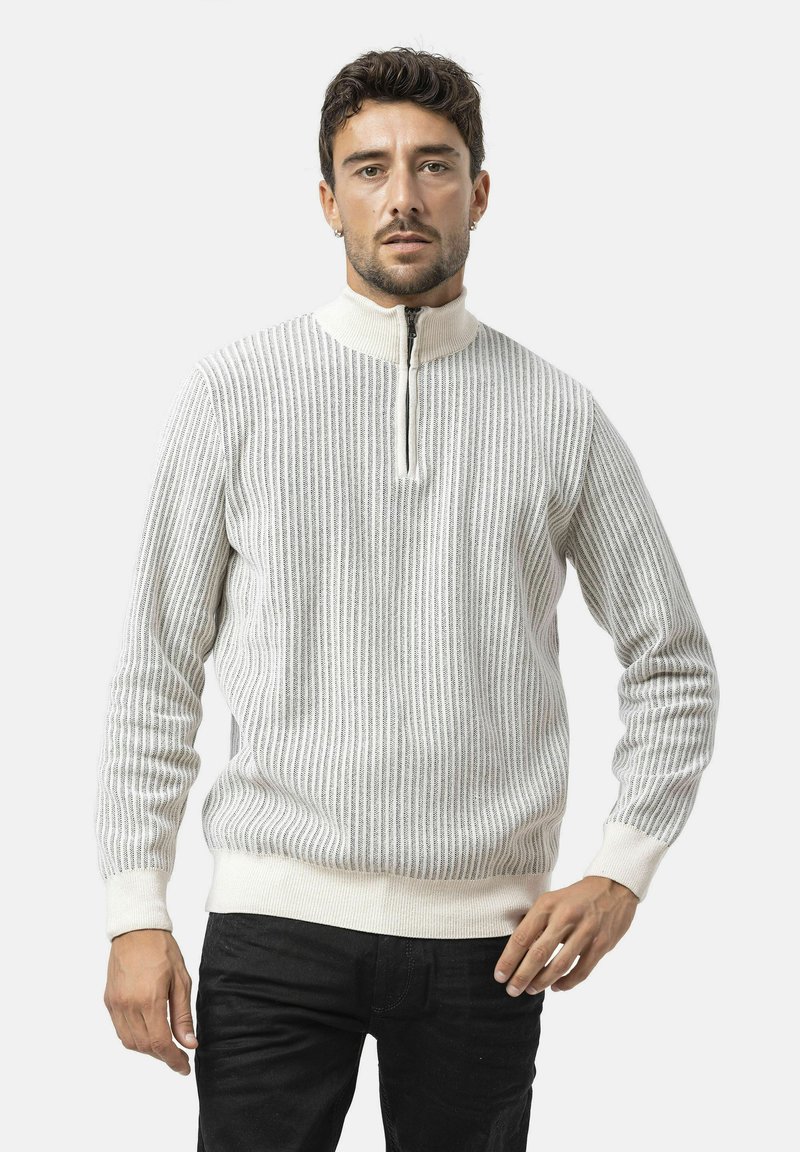 Hellgrauer Ripppullover mit einem halben Reißverschluss am Kragen, strukturiertem Strick und kontrastierendem cremfarbigen Saum und Bündchen, kombiniert mit schwarzen Hosen.