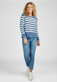 Blau-weiß gestreifter Pullover mit langen Ärmeln, lockerer Passform, geripptem Rundhalsausschnitt und Bündchen, kombiniert mit hellblauen Skinny-Jeans und weißen Sneakers.