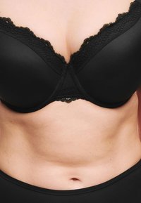 Sujetador acolchado negro con ribete de encaje a lo largo del escote, con una textura de tela suave y un diseño clásico que enfatiza el soporte y la cobertura.