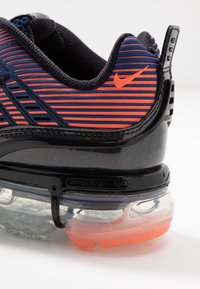 Nike-sneaker med ett marinblått och orange randigt mönster, texturerat mesh-ovandel och en genomskinlig luftdämpande sula med svarta accenter.