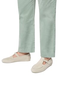 Scarpe slip-on in suede beige con una fascia sopra il piede, abbinate a pantaloni in cordura verde chiaro con taglio dritto e righe verticali.