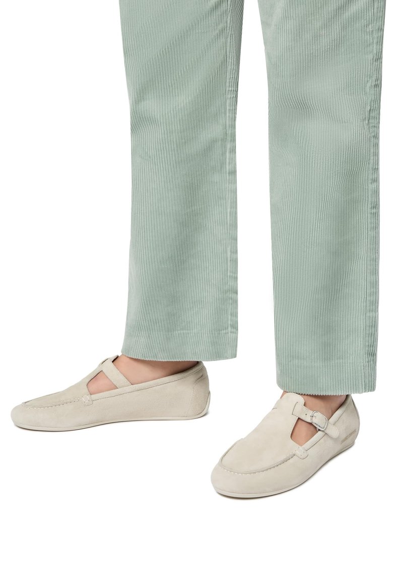Scarpe slip-on in suede beige con una fascia sopra il piede, abbinate a pantaloni in cordura verde chiaro con taglio dritto e righe verticali.