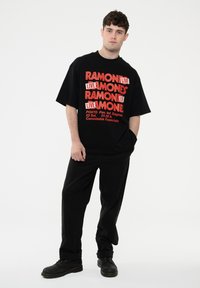 Black oversized T-shirt with bold red and white text featuring "RAMONES LIVE" and event details; paired with black pants and dark shoes.