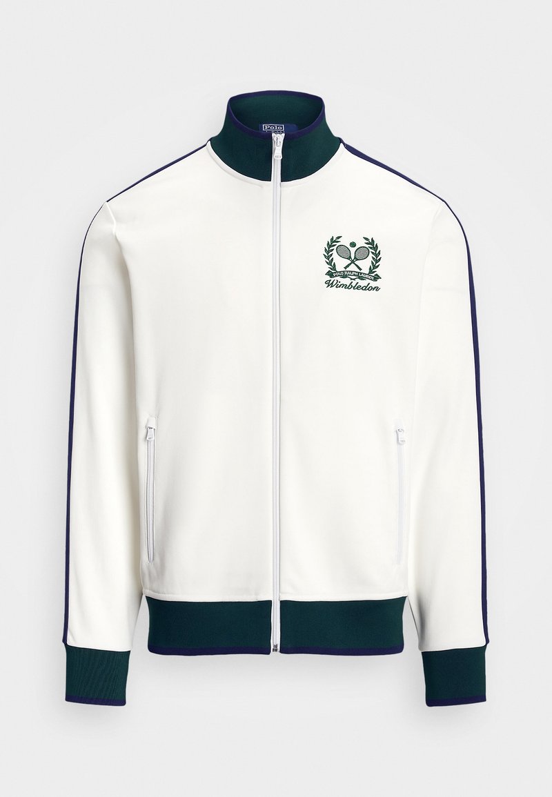 Bela jakna na zadrgo z zelenimi detajli, visokim ovratnikom in logotipom Wimbledona, ki vključuje teniško motiv. Vsebuje dve stranski žepki na zadrgo.