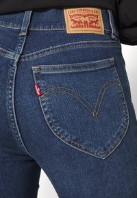 Dark blue denim jeans featuring a distinctive heart-shaped back pocket stitch, with a brown leather label and a small red tag.