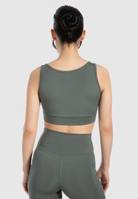 Tmavě zelená sportovní podprsenka s hladkým povrchem, širokými ramínky a přiléhavým střihem, doplněná o odpovídající legíny s vysokým pasem.
