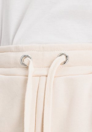 Beige Baumwoll-Sweatpants mit einem Kordelzug in der Taille, ausgestattet mit silbernen Ösen. Der Stoff hat eine glatte Textur und eine l�ässige Passform.