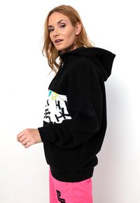 Schwarzer Fleece-Hoodie mit einem weißen und bunten Grafikpanel. Mit gerippten Bündchen und Saum sowie einem Reißverschluss-Halsausschnitt.