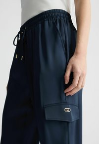 Pantalons navy à coupe décontractée, taille élastique, fermeture à cordon, poches latérales et accent en métal doré sur la poche cargo.
