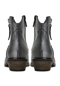 Botas de tobillo negras con tacón, con un acabado texturizado, que presentan un cierre con cremallera y costuras decorativas en la parte posterior. Tacón de madera grueso.