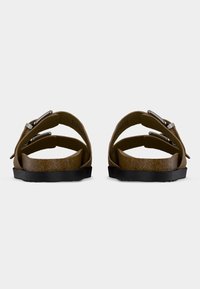 Ζευγάρι καφέ σανδάλια με ανοιχτά δάχτυλα, διπλούς ιμάντες με αγκράφες και πάτους από φελλό, απεικονιζόμενα από πίσω σε λευκό φόντο.
