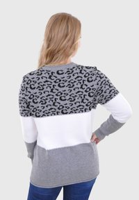 Grijze en witte sweater met een luipaardprintpatroon, textuur breisels, lange mouwen en een ronde hals. Accenten in het zwart.