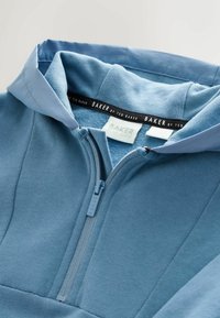 Felpa con cappuccio azzurro chiaro con cerniera frontale, realizzata in tessuto morbido, con cappuccio e colletto a contrasto. L'interno presenta una texture liscia. L'etichetta riporta "BAKER by Ted Baker".