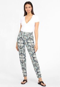 Spodnie z wzorem o dopasowanym kroju, z abstrakcyjnym wzorem w kolorach niebieskim, czarnym i białym, wykonane z lekkiej tkaniny. Noszone z płaskimi sandałami.