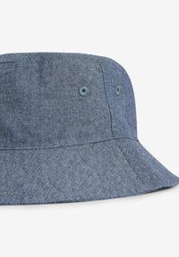 Dunkelblaues Denim-Bucket-Hat mit breiter Krempe und subtiler Textur. Verfügt über kleine Ösen zur Belüftung. Nahtdetails um die Krone.