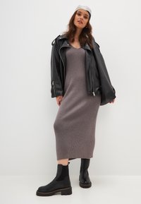 Chaqueta de cuero negra de moto sobre un vestido de punto acanalado gris, combinada con botas negras de tobillo chunky. El conjunto combina diferentes texturas y formas ajustadas.