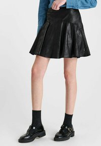 Zwarte leren rok met uitlopende stijl, zachte textuur en hoge tailleband. Gecombineerd met zwarte schoenen en geribde zwarte sokken.