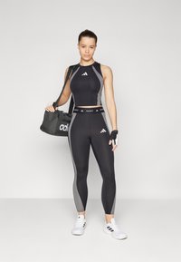 Svart sportstopp og tights med grå detaljer, tight passform, og Adidas-merke; inkluderer en svart treningsbag og hansker.