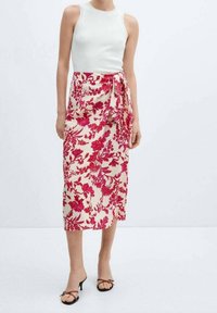 Gonna midi floreale color crema con audaci motivi rosa. Presenta un design a portafoglio con un nodo laterale. Accompagnata da un top bianco aderente.